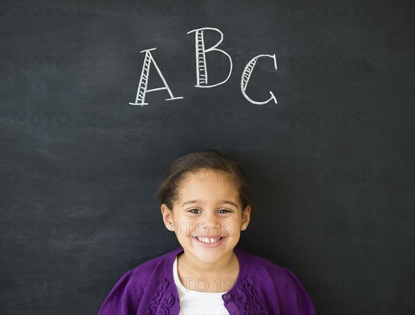 Hispanic girl standing under 'ABC' on chalkboard