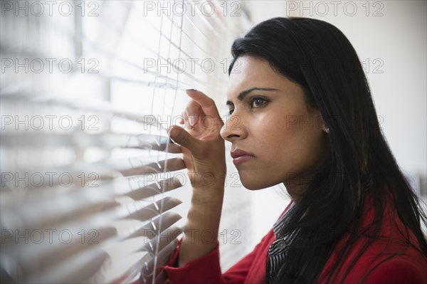 Indian businesswoman peering through blinds in office