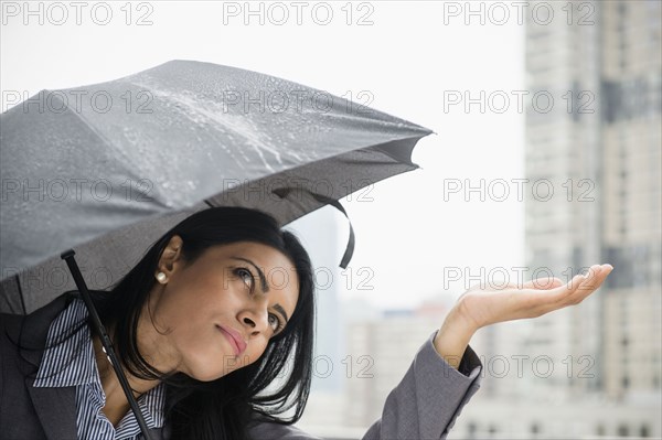 Indian businesswoman feeling rain from under umbrella