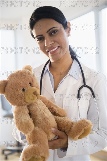 Indian doctor holding teddy bear in office