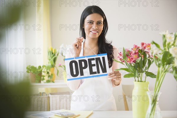 Indian florist holding 'open' sign