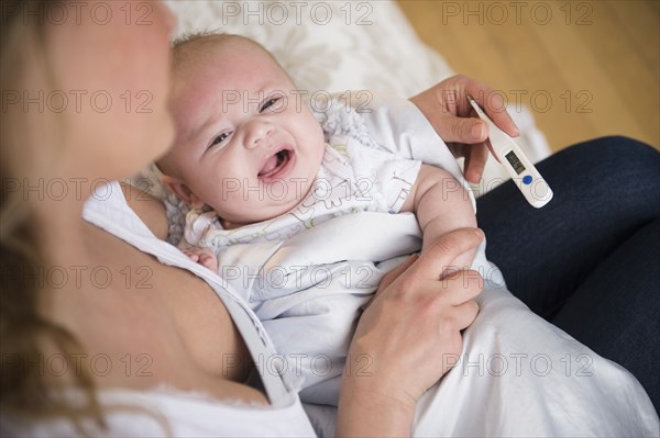 Caucasian mother taking crying baby's temperature