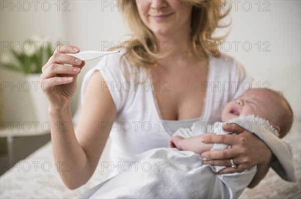 Caucasian mother taking crying baby's temperature