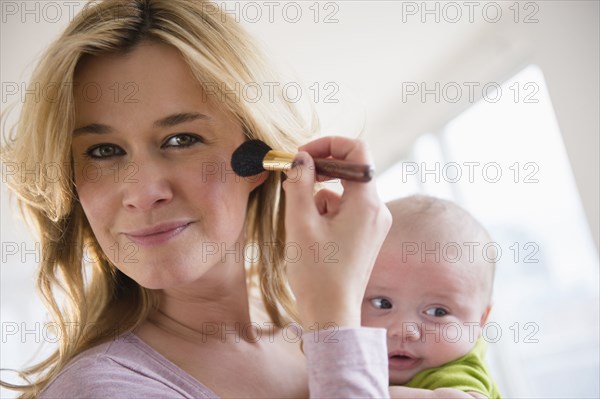 Caucasian mother with baby applying makeup