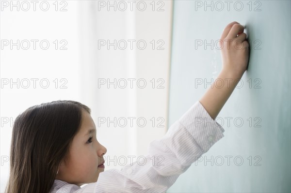 Mixed race girl writing on chalkboard