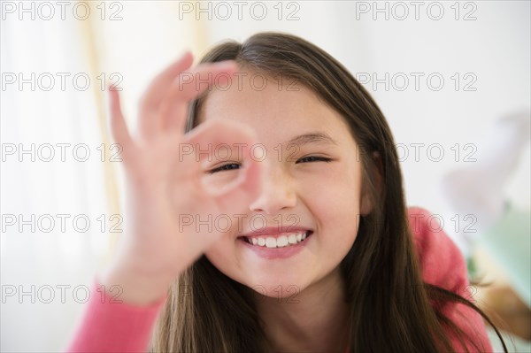 Mixed race girl making O.K. sign with fingers