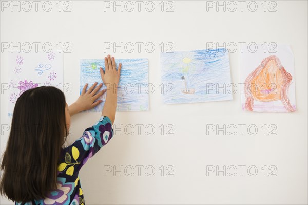 Mixed race girl hanging drawings on wall