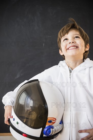 Hispanic boy holding space helmet in classroom