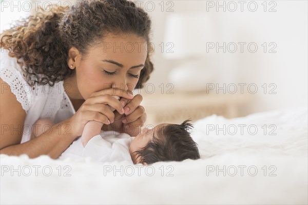 Hispanic mother playing with infant on bed