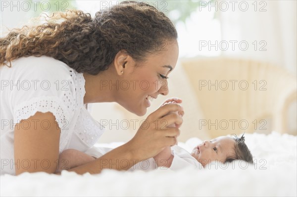 Hispanic mother playing with infant on bed