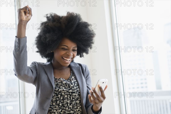 Mixed race businesswoman holding cell phone and cheering