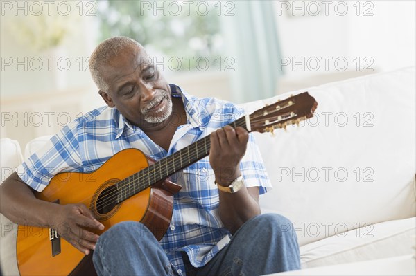 Black man playing guitar on sofa