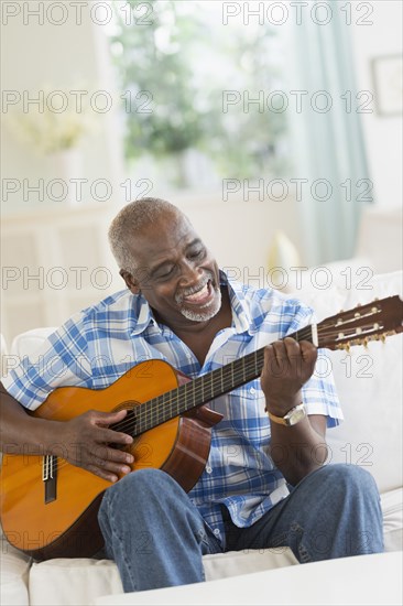 Black man playing guitar on sofa