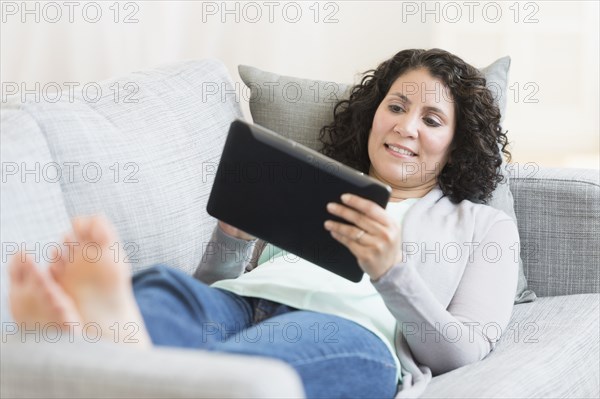 Hispanic woman using digital tablet on sofa