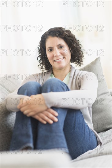 Hispanic woman hugging her knees on sofa