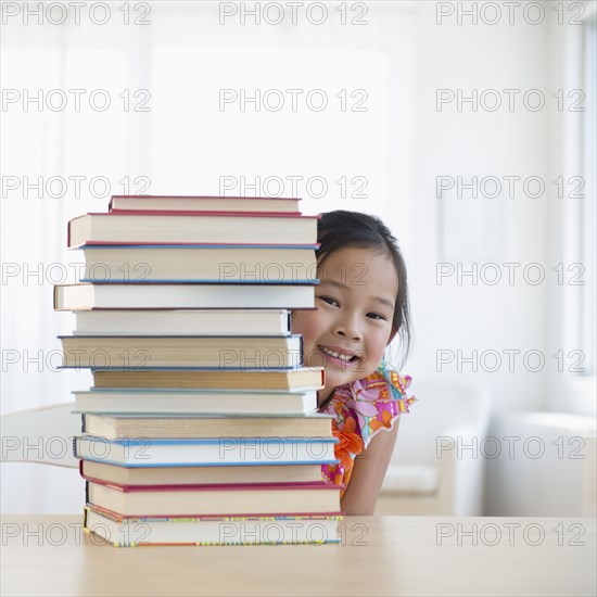 Korean girl peeking from behind stack of books