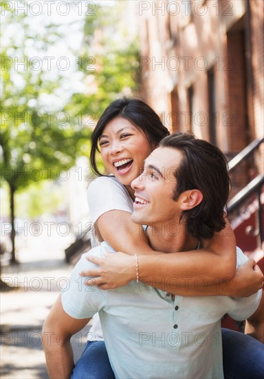 Man carrying girlfriend piggyback on urban sidewalk