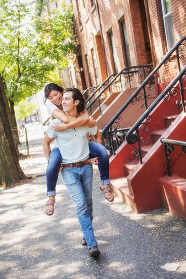 Man carrying girlfriend piggyback on urban sidewalk