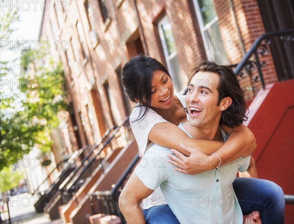 Man carrying girlfriend piggyback outside brownstones