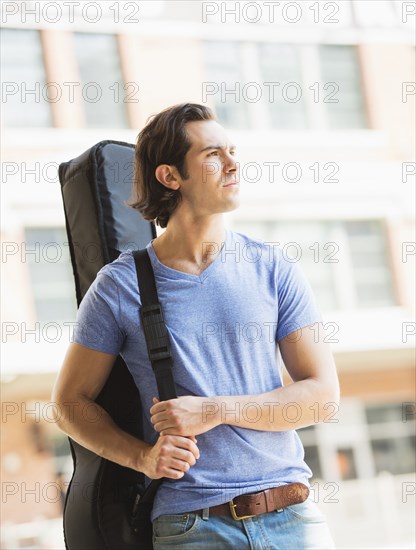 Caucasian man carrying guitar case on urban street