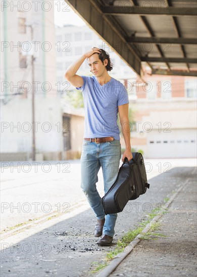 Caucasian man carrying guitar case on city street