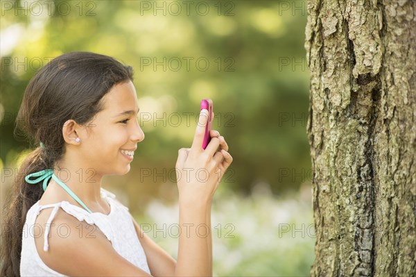 Mixed race girl photographing tree trunk with camera phone