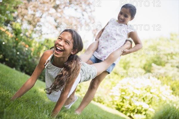 Mixed race girls playing wheelbarrow in backyard