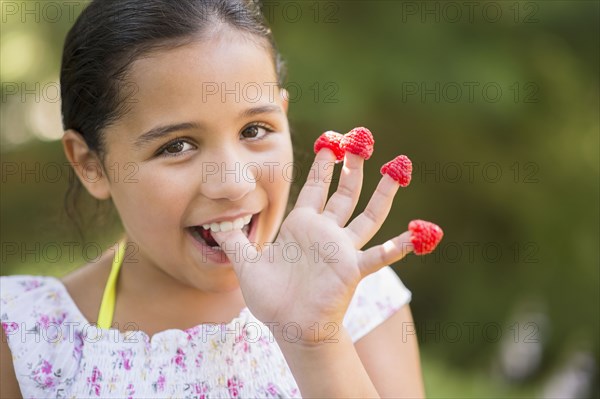 Mixed race girl eating raspberries on fingers outdoors