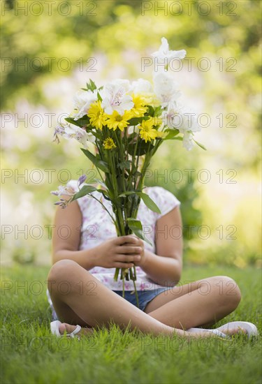 Mixed race girl holding bouquet of flowers in grass