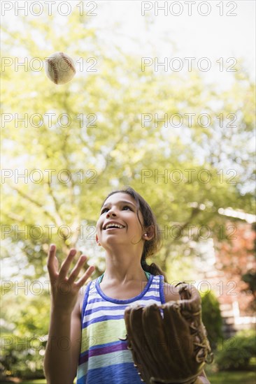 Mixed race girl playing with baseball and mitt outdoors