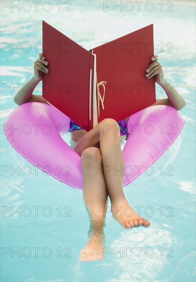 Mixed race girl reading in swimming pool
