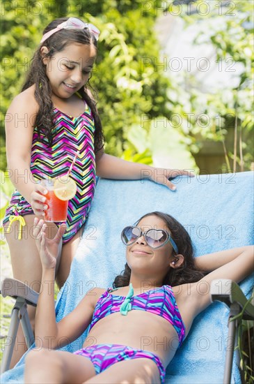 Mixed race girl serving sister juice at poolside