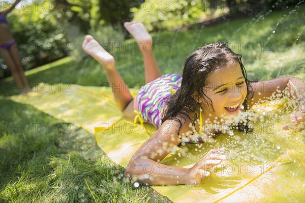 Mixed race girls playing on slip and slide in backyard
