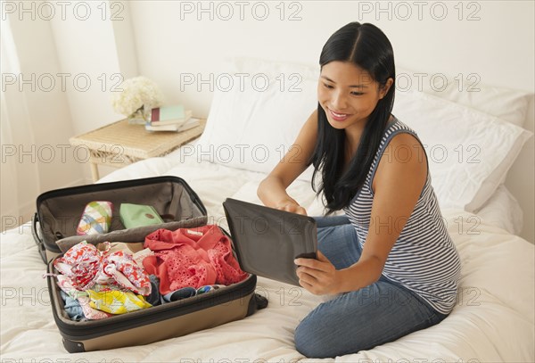 Chinese woman using digital tablet and packing suitcase