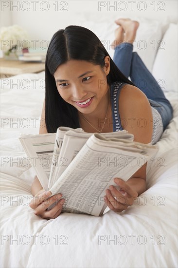 Chinese woman reading newspaper on bed