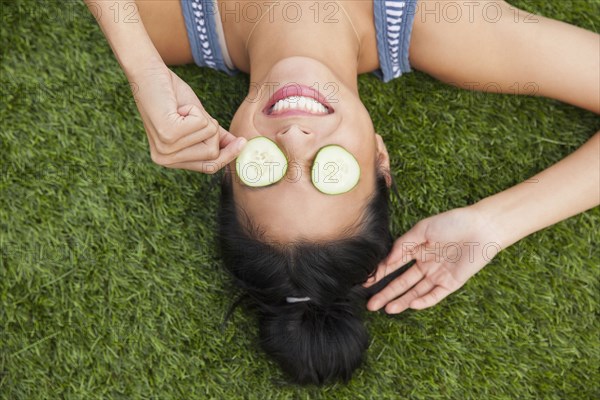 Chinese woman with cucumbers on eyes laying in grass