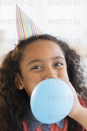 Mixed race girl inflating balloon at birthday party