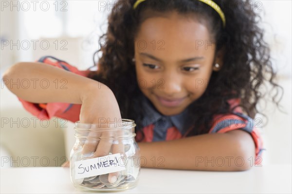 Mixed race girl putting coins in summer savings jar