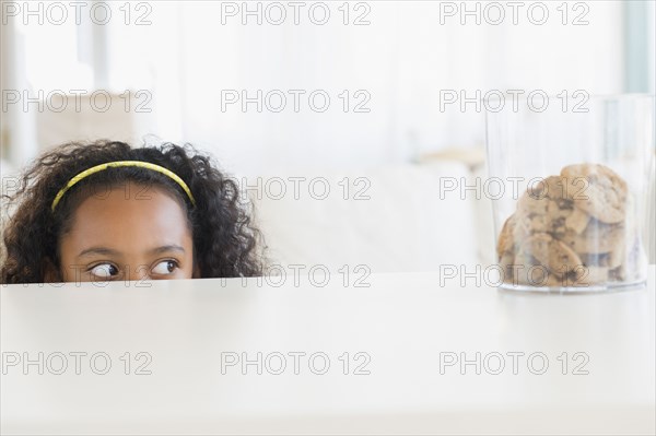 Mixed race girl peering at cookie jar