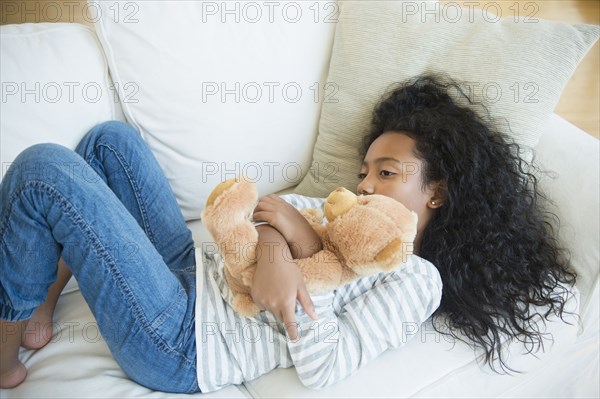 Mixed race girl hugging teddy bear on sofa