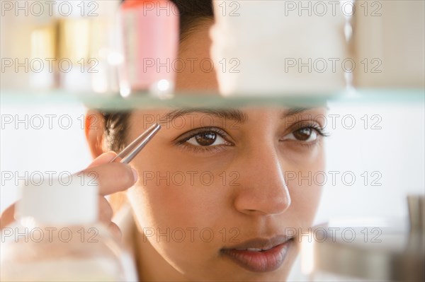 Close up of Asian woman tweezing eyebrows