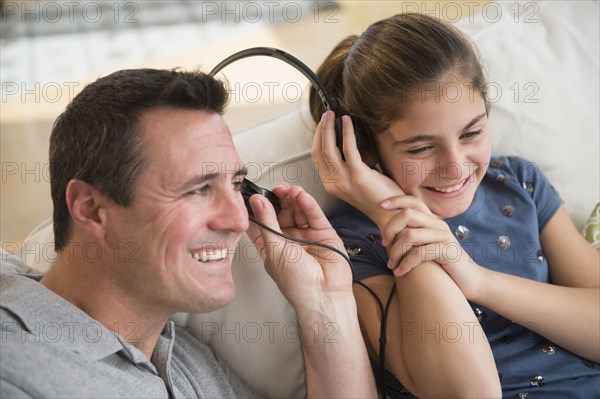 Smiling Caucasian father and daughter sharing headphones