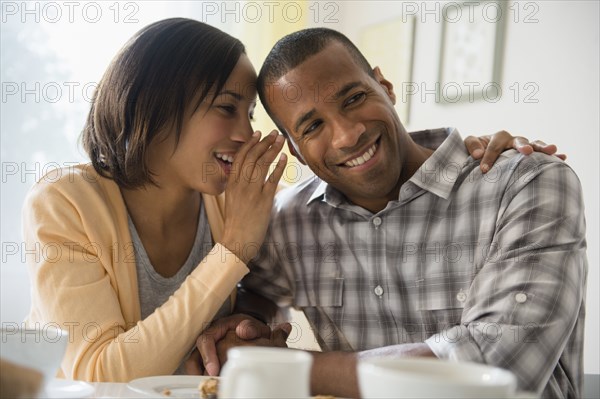 Woman whispering in boyfriend's ear at table