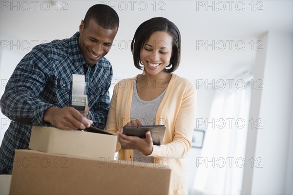 Couple with digital tablet taping up moving boxes