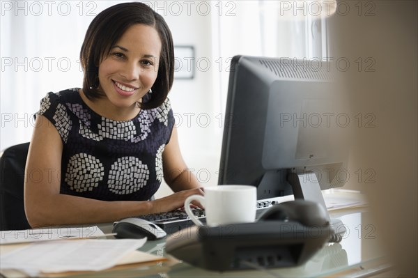 Portrait of smiling mixed race businesswoman at computer