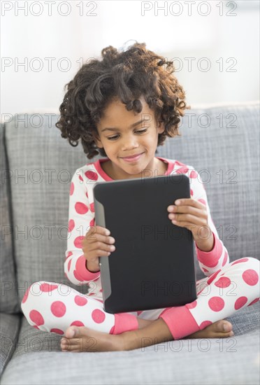 African American girl in pajamas using digital tablet on sofa