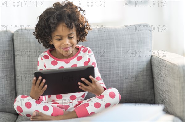 African American girl in pajamas using digital tablet on sofa