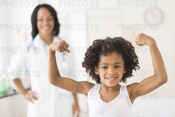 Portrait of African American girl flexing muscles in doctor's office