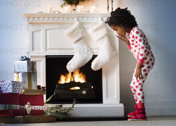 Surprised Black girl in pajamas looking down at Christmas gifts