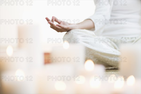 Hispanic woman meditating in lotus position near lit candles
